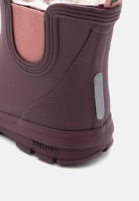 Lila gummistövlar med rosa textilaccent, strukturerad design, en reflekterande remsa och en märkes-sula. Har mjukt foder vid öppningen.