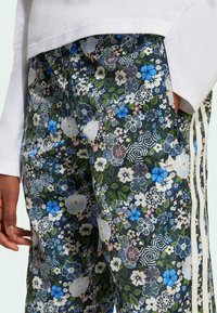 Joggingové nohavice s kvetinovým vzorom v tmavozelenej farbe, s modrými a ružovými kvetmi, bočnými vreckami a smotanovými prúžkovými detailmi.