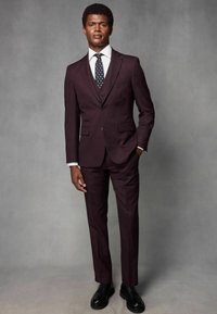 Bordo odijelo sa slim fit krojem, s dugim rukavima, usklađenim hlačama, bijelom košuljom i kravatom s točkicama. Crne cipele za odijela upotpunjuju izgled.