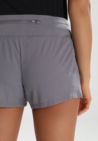 Grå atletiska shorts i ett slätt, lättviktigt tyg. Har en bred midja, perforerade sidor för andningsförmåga och en platt fåll.