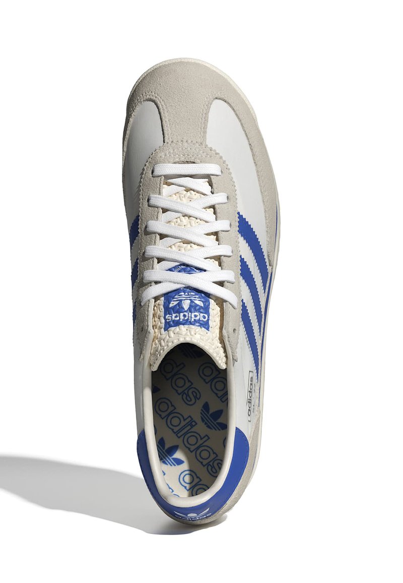 Białe i szare zamszowe sneakersy z niebieskimi paskami, teksturowanym czubkiem i białymi sznurowadłami. Logo Adidas widoczne na języku i wkładce.