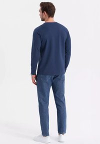 Long-sleeve navy T-shirt with a white and red collar, paired with light blue jeans and white sneakers. Simple design with minimal accents.