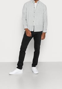 Camisa de botones a rayas en verde claro y blanco, combinada con jeans negros y zapatillas blancas. Presenta mangas largas y detalles de botones.