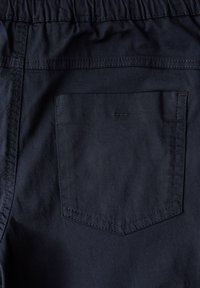 Pantalones cortos de tela azul marino con cintura elástica, que presentan un único bolsillo trasero de forma cuadrada y un detalle de costura limpia.