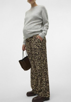 Un pull en tricot gris clair, un pantalon large à motif léopard en beige et marron, des chaussures massives marron foncé et un petit sac à épaule noir.