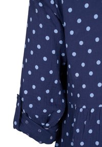 Marineblå bluse med lyseblå polka prikker. Har rullede ærmer og indsamlet talje, lavet af tekstureret stof.