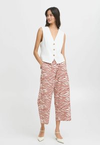 Canotta bianca senza maniche con scollatura a V profonda e tre bottoni dorati abbinata a pantaloni culotte con un motivo a strisce zebra rosse.