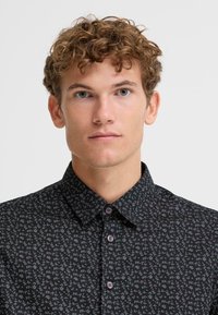 Camicia nera con bottoni, caratterizzata da un sottile motivo floreale in colori tenui, con colletto classico e bottoni lilla.