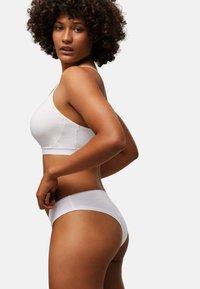 Bralette de algodón blanco con escote redondo, combinado con braguitas hipster blancas, con un borde elástico festoneado. Textura suave, diseño minimalista.