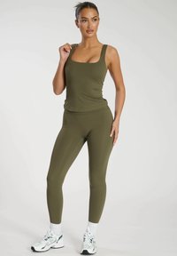 Canotta sportiva verde oliva con scollatura quadrata, abbinata a leggings coordinati. Entrambi presentano una texture liscia e un design aderente.