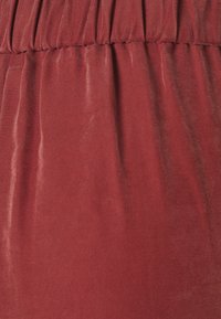 Tissu rouge à texture lisse, présentant un design plissé à la taille et des rayures diagonales subtiles.