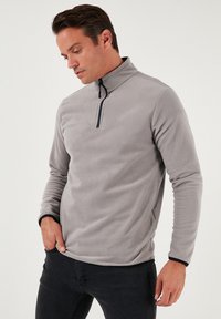 Grå fleece-pullover med opretstående krave og halvlangt lynlås. Har lange ærmer med sorte accenter og en blød tekstur.