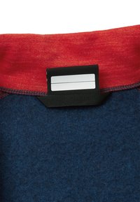 Rød stofkant øverst, mørkeblå uldkrop, med et sort mærke der indeholder en hvid label til information eller størrelse.