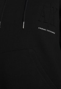 Felpa nera con cappuccio e grande logo in rilievo "AX" con "ARMANI EXCHANGE" stampato in bianco. Presenta lacci con punte metalliche e una tasca a marsupio.