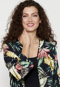 Květinová kimono bunda v tmavě modré barvě s výraznými tropickými listovými vzory. Má volný střih, široké rukávy a lehký materiál.