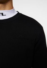 Felpa nera con collo a costine e logo ricamato "J.LINDEBERG" nello stesso colore, caratterizzata da un tessuto testurizzato e un design aderente.