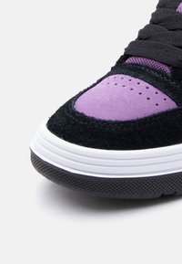 Κοντινό πλάνο της μύτης αθλητικού παπουτσιού με μωβ σουέτ, μαύρες υφασμάτινες επικαλύψεις, μαύρα κορδόνια και λευκή ενδιάμεση σόλα με μαύρη λαστιχένια εξωτ ερική σόλα.