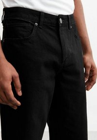 Jeans in denim nero con una vestibilità classica, dotati di chiusura a bottone, passanti per cintura e tasche anteriori. Tessuto liscio con cuciture minime visibili.