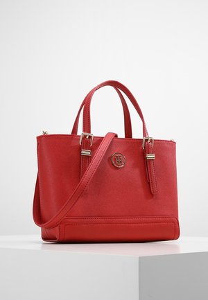 Rote Lederhandtasche mit zwei oberen Griffen, einem abnehmbaren Schulterriemen, goldenen Schnallen und einem runden Logoemblem auf der Vorderseite.