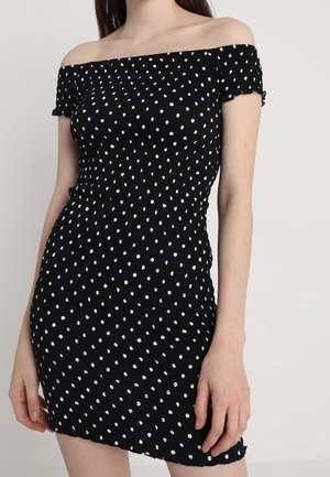 Czarna sukienka z odkrytymi ramionami w białe groszki, o dopasowanym, teksturowanym kroju i marszczonym materiale zapewniającym elastyczność.