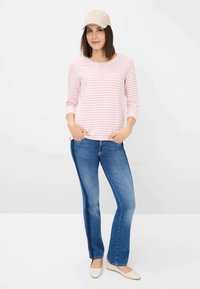 Ein rosa und weiß gestreiftes Langarmhemd, blaue Schlagjeans und eine beige Mütze mit einem blauen Schirm, ergänzt durch beiges flaches Schuhwerk.