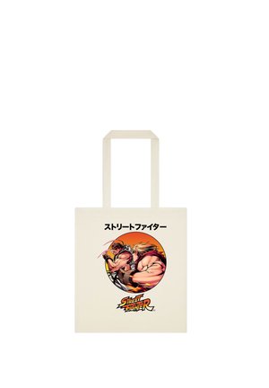 Beżowa torba typu tote z dwoma muskularnymi wojownikami w pozie akcji wewnątrz pomarańczowego koła z japońskim tekstem i logo Street Fighter poniżej.
