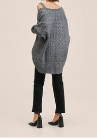 Grauer, übergroßer Strickpullover mit Kabelmuster; verfügt über ein schulterfreies Design und gerippte Bündchen, kombiniert mit schwarzen, geraden Hosen und Absatzschuhen.