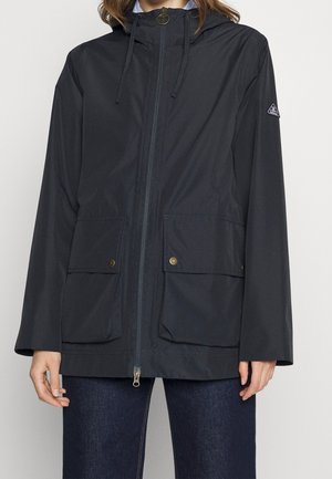 Granatowa kurtka przeciwdeszczowa wykonana z lekkiego materiału, z zamkiem błyskawicznym z przodu, regulowanym kapturem, dwiema przednimi kieszeniami z zapięciami na napy oraz luźnym krojem.