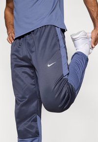 Ανδρικό αθλητικό παντελόνι Nike σε σκούρο μπλε με ανοιχτό μπλε λεπτομέρειες, με λεία υφή, φερμουάρ στα μανσέτα και λογότυπο στο μηρό.