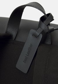 Svart läderbagagetagg med präglingen "Ekte läder" fäst vid handtaget av en svart tyg- och läderväska.