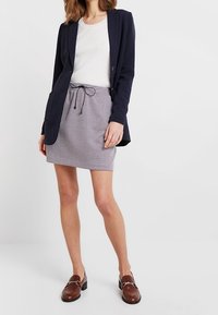 Námořnický blazer, bílý žebrovaný top, kostkovaná šedá sukně s šňůrkou a hnědé mokasíny. Oblečení má přiléhavý střih.