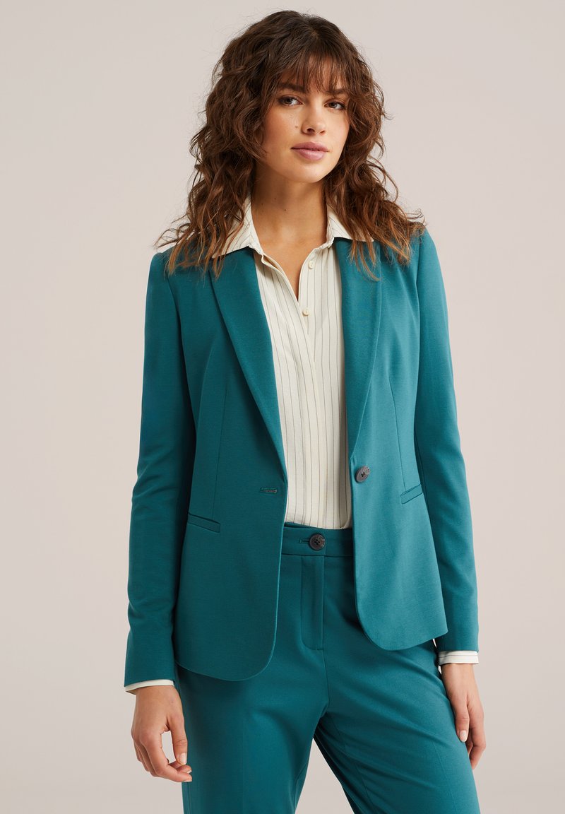 Turkizni blazer iz mehkega blaga z zarezanimi reverji, dvema gumboma in sprednjimi žepi, kombiniran z belo progasto bluzo.