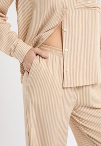 Zestaw do noszenia w domu w paski w kolorach beżowym i białym; składa się z koszuli na guziki i spodni z elastycznym paskiem z napisem „DOG LOVER”. Miękka tkanina, luźny krój.