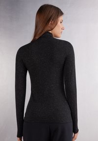 Sort langærmet turtle neck skjorte med en tætsiddende silhuet, lavet af tekstureret stof med subtile prikker over det hele.
