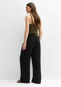 Groene geribbelde tanktop met dunne bandjes, gecombineerd met losse zwarte wijde broekspijpen, met een gestructureerde stof en elastische tailleband.
