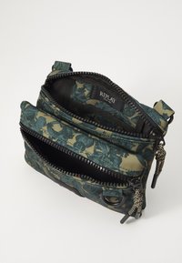 Stofftasche mit floralem Muster in Grün und Beige, mit mehreren Reißverschlussfächern, schwarzer Hardware und einem gewebten Riemen.