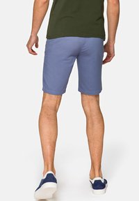 Męskie szorty w jasnoniebieskim kolorze, wykonane z mieszanki bawełny, sięgające do kolan, o prostym wzornictwie z tylnymi kieszeniami, w połączeniu z granatowymi butami typu slip-on.