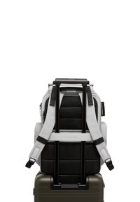 Un sac à dos noir et gris avec un dos rembourré, des bretelles ajustables et une poignée supérieure, reposant sur une valise rigide avec une finition métallique.