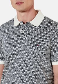 Polo de color marino y blanco con un patrón, con cuello, que presenta un diseño geométrico, dos botones y un pequeño logotipo en rojo en el pecho.