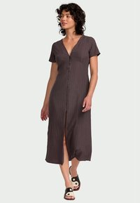 Braunes, knielanges Kleid mit kurzen Ärmeln, V-Ausschnitt, vertikalen Streifen und Knopfleiste. Kombiniert mit schwarz-weißen Sandalen.