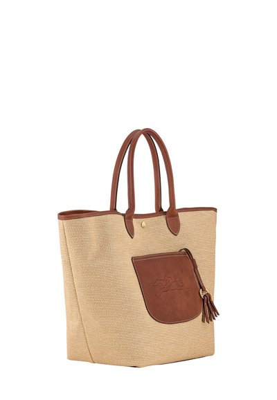 Tan woven tote bag with brown leather accents, features dual handles, a front pocket, and a tassel detail. Smooth texture with stitching.