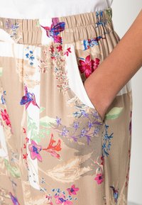 Leichte, floral bedruckte Hosen mit elastischem Bund, beiger Grundfarbe, lebhaften roten, blauen und rosa Blumen, mit seitlichen Taschen.