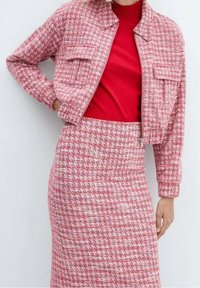 Veste à carreaux rose et blanche avec deux poches avant, associée à un haut rouge ajusté et une jupe crayon assortie. Tissu texturé sur l'ensemble.