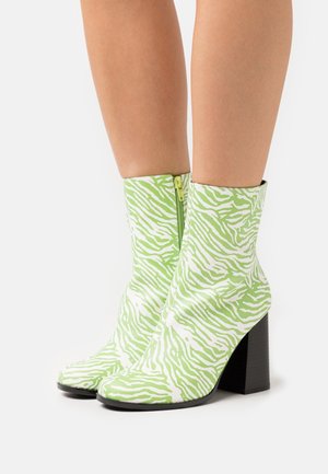 Botas de tobillo de estampado de cebra verde y blanco con cierre de cremallera, que presentan un tacón ancho negro y una textura lisa y brillante.
