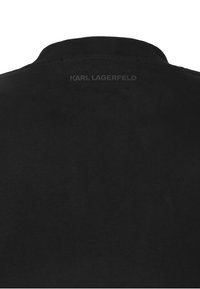 Musta puuvillainen t-paita pyöreällä kaula-aukkolla. Selässä hienovarainen, kohokuvioitu "KARL LAGERFELD" -merkintä. Pehmeä pinta ja yksinkertainen muotoilu.