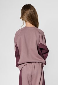 Mauvefärgad tvåfärgad tröja med raglanärmar och en avslappnad passform, kombinerad med matchande mauvefärgade byxor. Mjukt tyg med en slät textur.