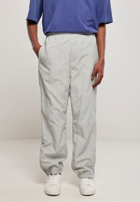 Ljusgrå nylonbyxor med elastisk midja, sidofickor och elastiska muddar, designade för en avslappnad passform. Bärs med vita sneakers.