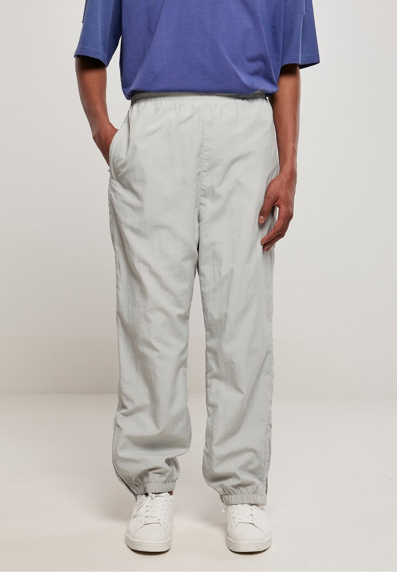 Ljusgrå nylonbyxor med elastisk midja, sidofickor och elastiska muddar, designade för en avslappnad passform. Bärs med vita sneakers.
