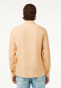 Camicia a maniche lunghe in pesca chiaro realizzata in un tessuto texturizzato. Presenta un colletto classico, polsini con bottoni e un orlo leggermente curvato.