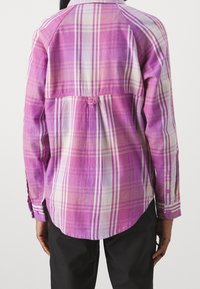 Long-sleeve button-up shirt in pink plaid, featuring white and purple accents, a curved hem, and a back pleat for added detail.
